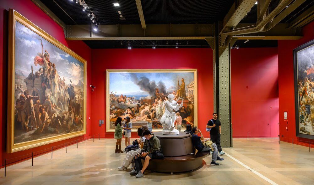 Museums in Paris: A red room in the Orsay Museum in Paris with people on a central bench