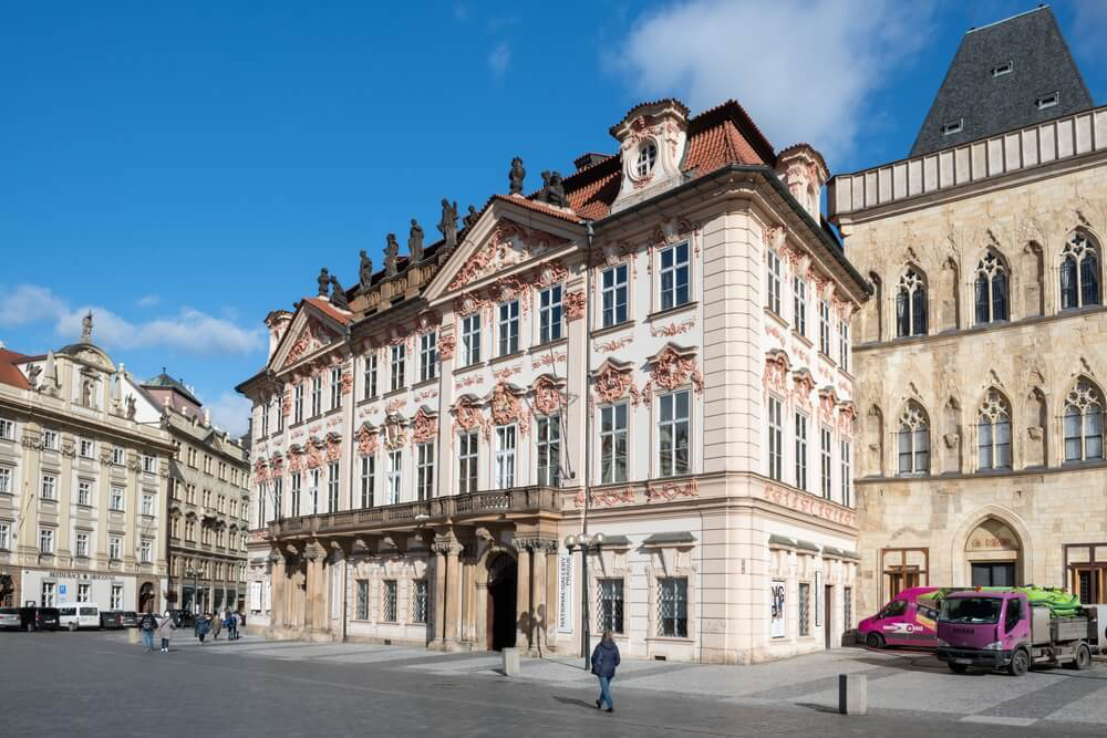 National Gallery: A white stone building with pink detailing on a street corner of Prague