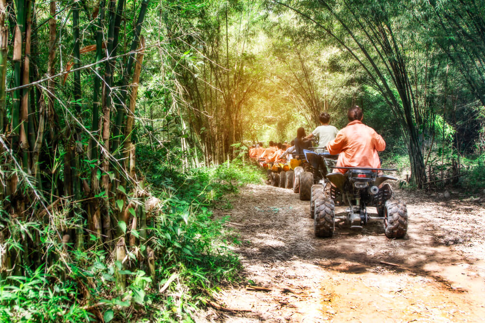 A group of people ride ATVs through a lush, green, Caribbean jungle.