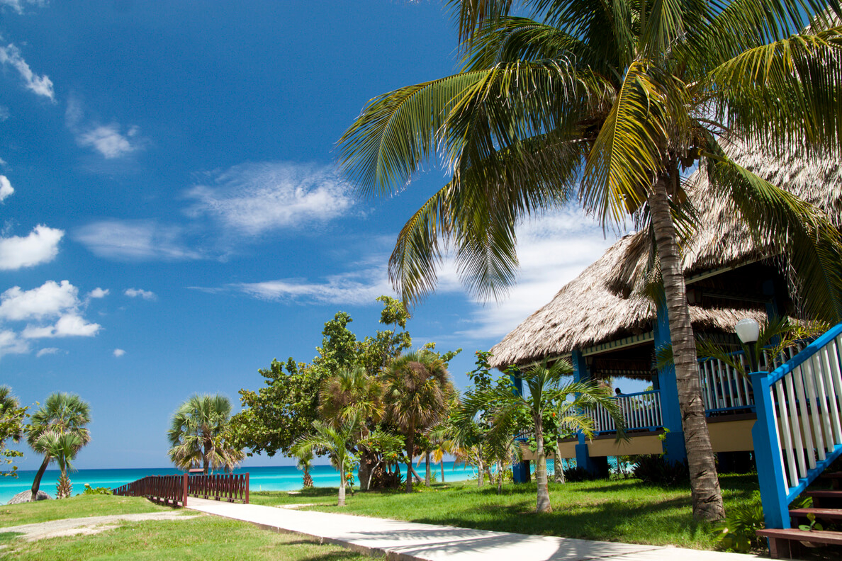 Places to visit in Cuba: A blue and white palm-roofed beach hut on a grassy track