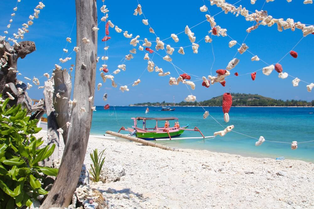 Gili Islands: White sand beach with pink fishing boat in the sea