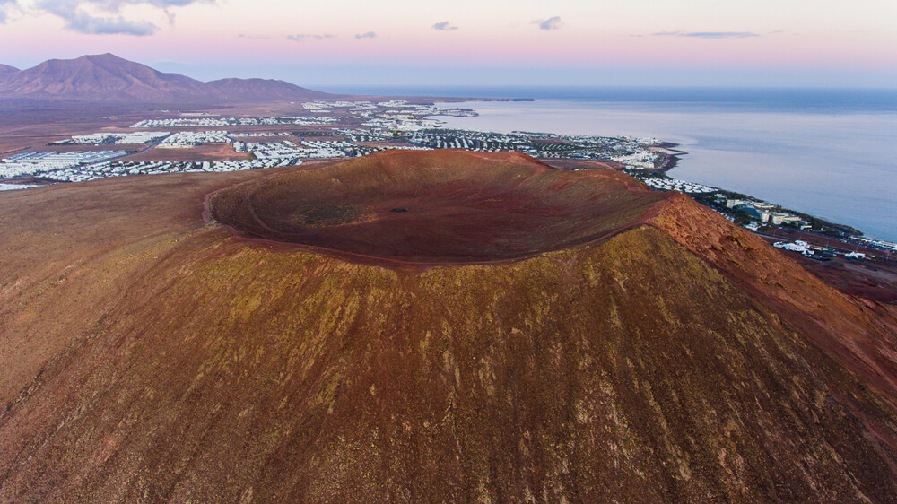 Playa Blanca Urlaub: Vulkankrater des Montaña Roja mit dem Ort im Hintergrund.
