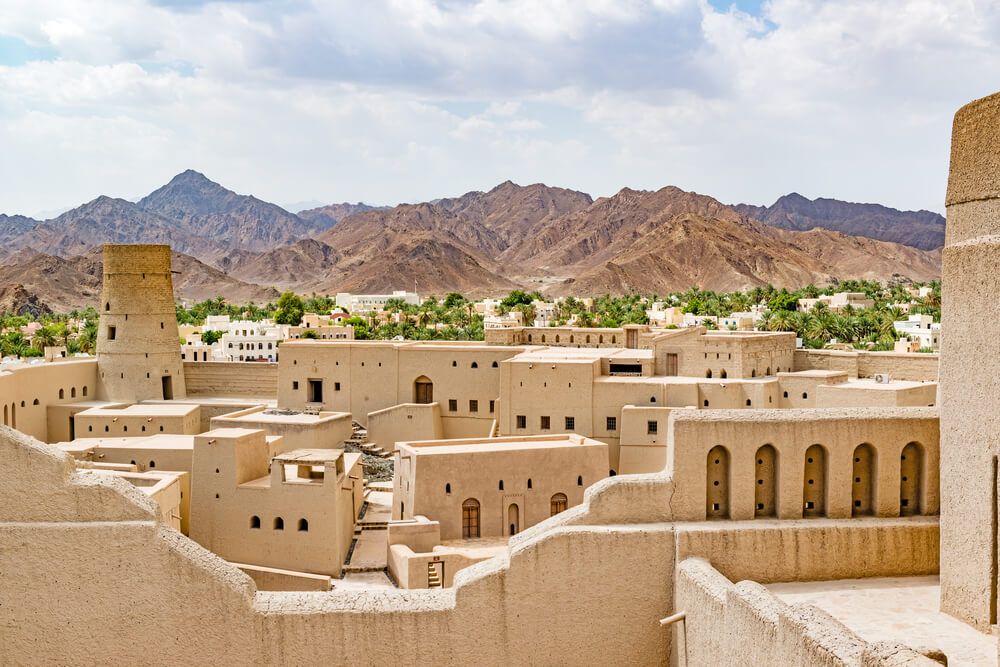 Festung im Oman mit Palmenhain und Bergen im Hintergrund.