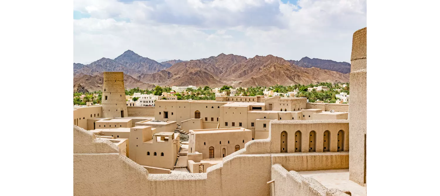 Festung im Oman mit Palmenhain und Bergen im Hintergrund.