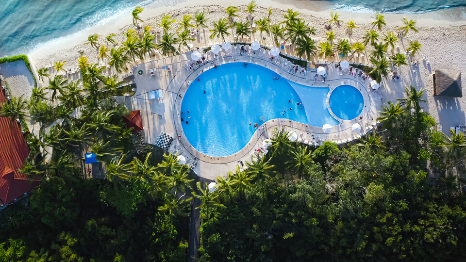 Reiseziele für Flitterwochen: Swimmingpool und Strand auf Isla Cozumel aus der Vogelperspektive.