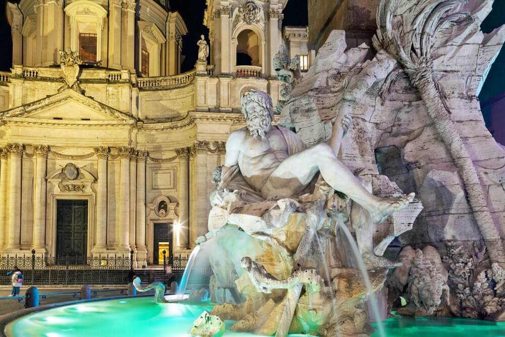Beleuchteter Brunnen des Piazza Navona in Rom bei Nacht.