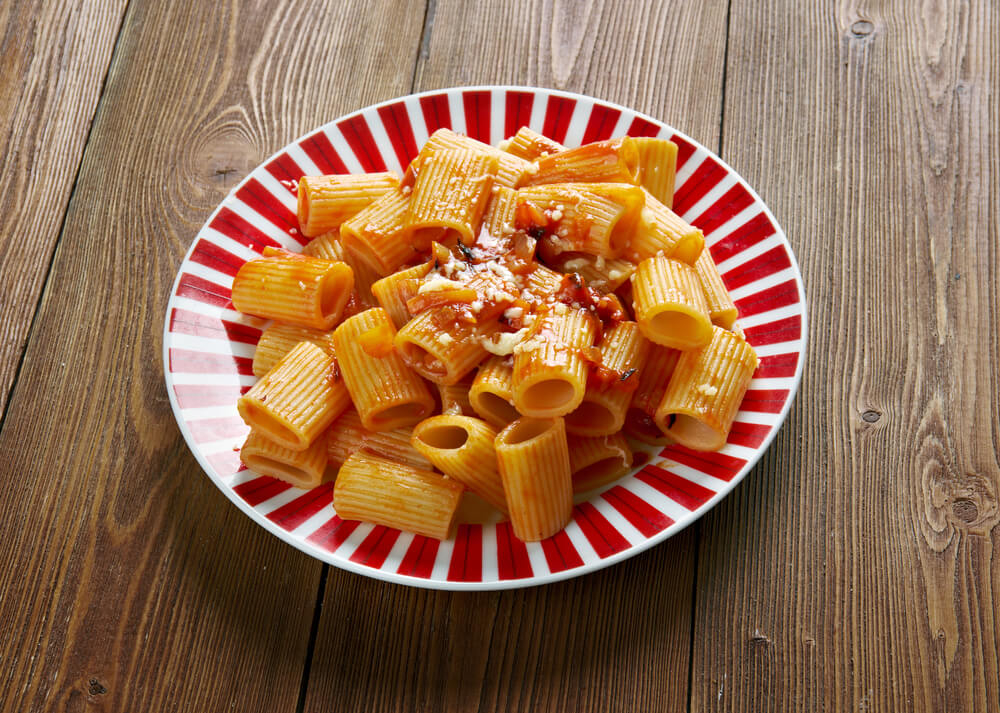 Rigatoni con la Pajata: A red and white striped plate full of rigatoni pasta