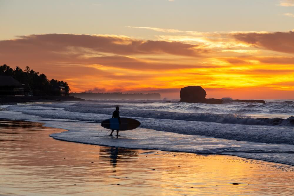 El Salvador Urlaub: Surfer am Strand von El Tunco mit hohen Wellen in der Dämmerung.