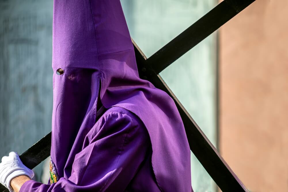 Semana Santa: A man wearing a purple hooded cloak carrying a cross