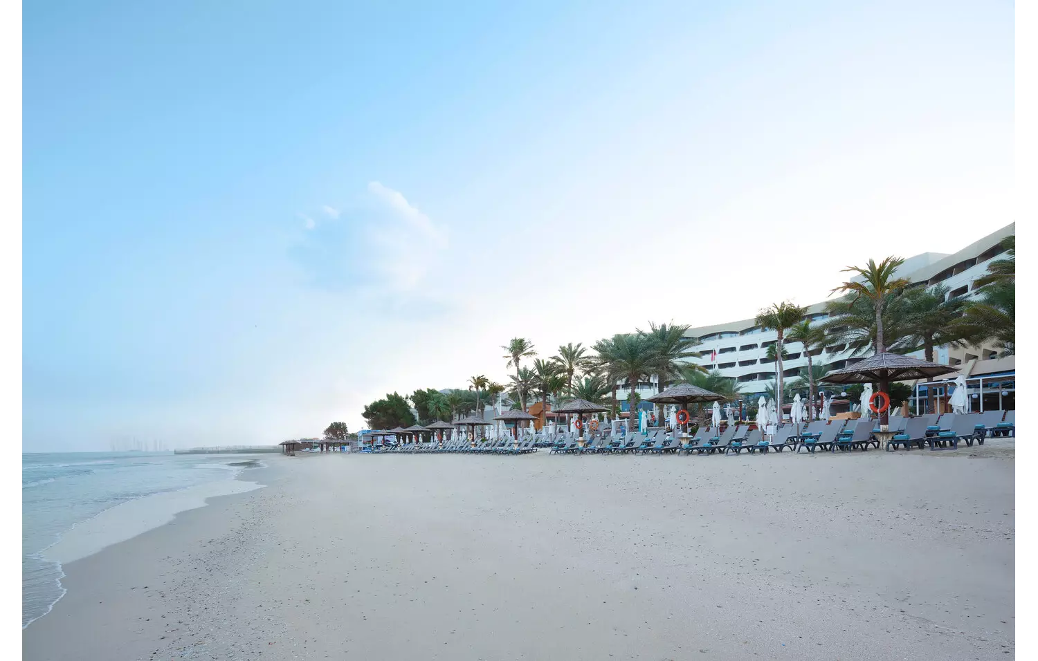 Sharjah-Urlaub: Hotelstrand mit Liegen und Palmen.