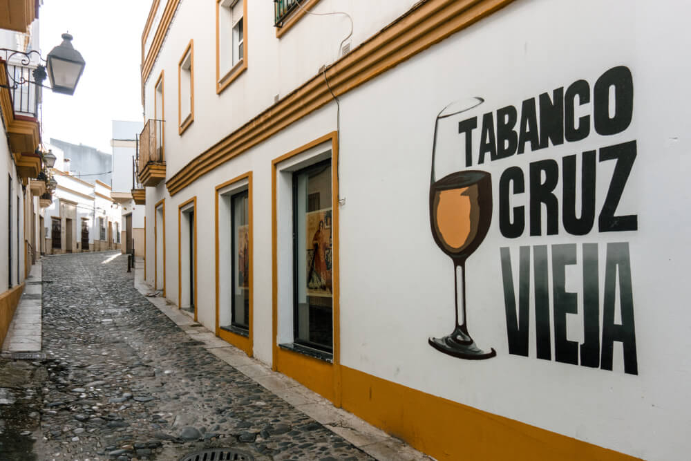 Jerez Street: A cobbled pathway with a white wall and painted bar sign