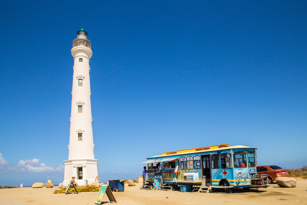 Aruba: The white California lighthouse on the beach with a colourful food truck