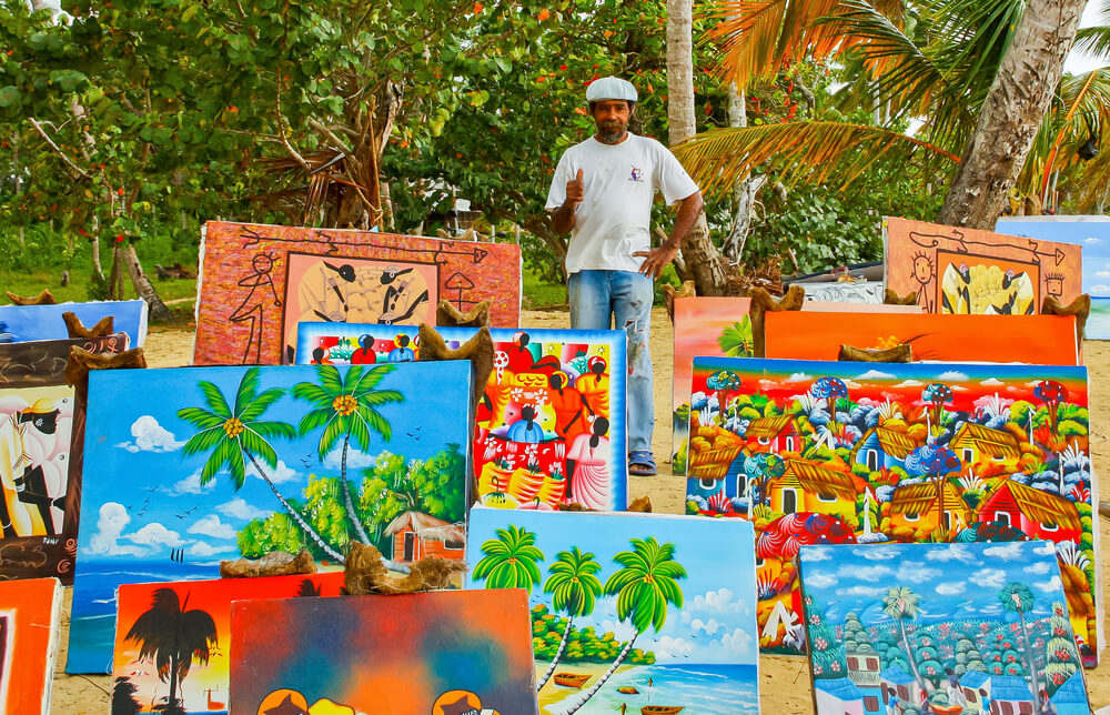 Ein Mann stellt dominikanische Malerei an einem Strand aus.