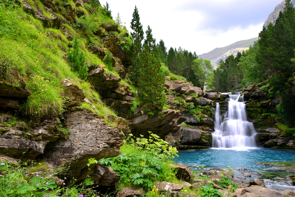 Spanische Pyrenäen: Wasserfall zwischen Felsen und grüner Vegetation.