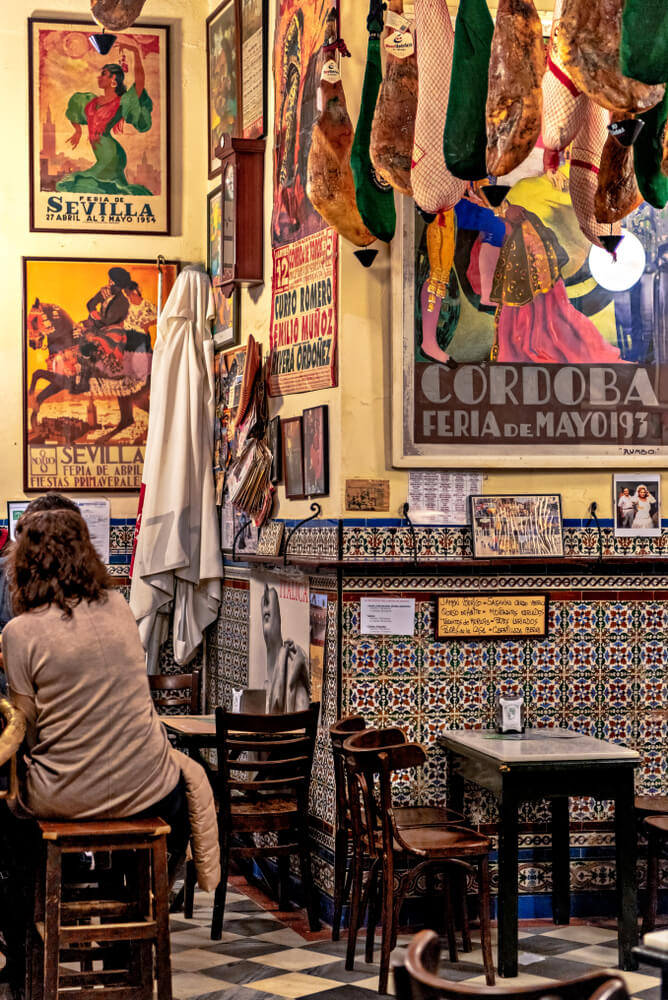 Mosaic tiled walled Spanish tapas bar with hanging hams and flamenco art