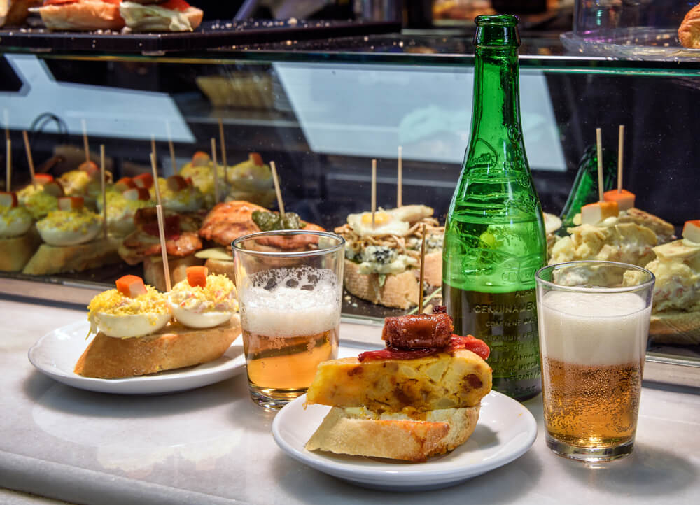 A close up of two beers and a plate of tapas in a bar