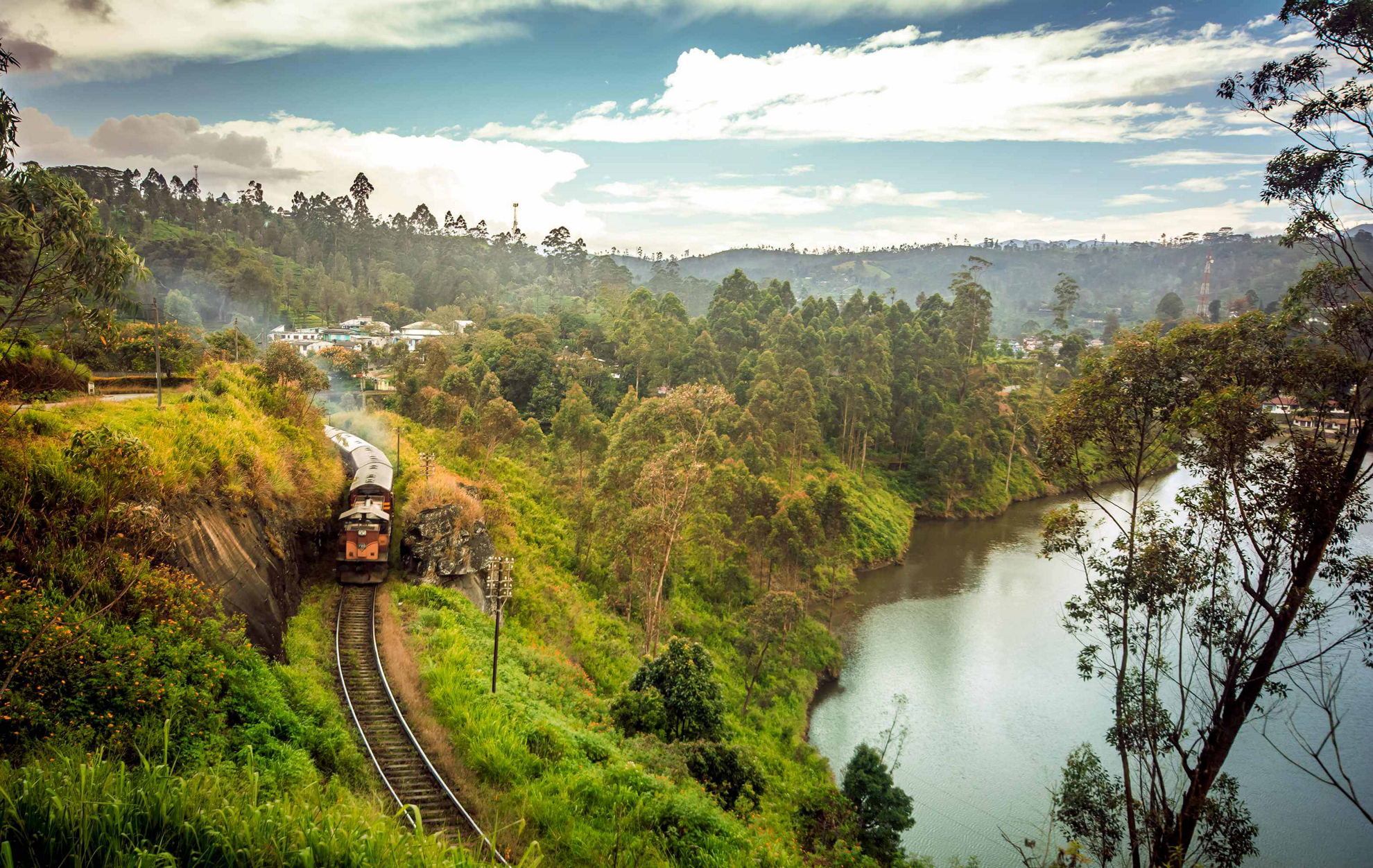 Sri Lanka mit dem Zug: Fahrt entlang eines Dorfes und eines Sees inmitten von üppiger Vegetation.