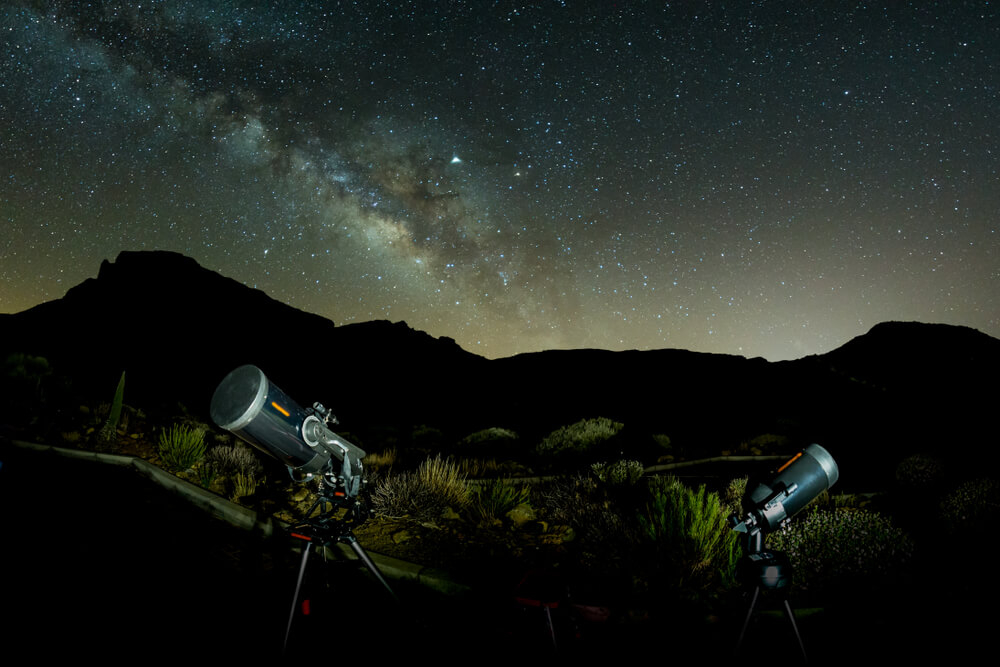 Stargazing in Tenerife: A starry sky and mountain range with professional telescopes