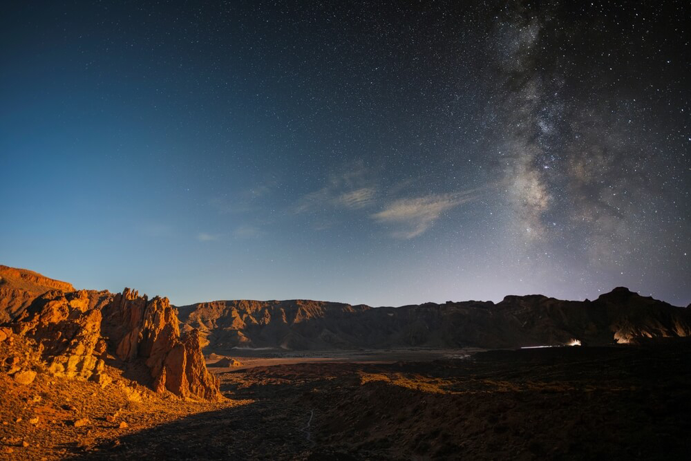 Landschaft im Teide Nationalpark zu einer Hälfte bei Tageslicht, zur anderen mit Sternenhimmel