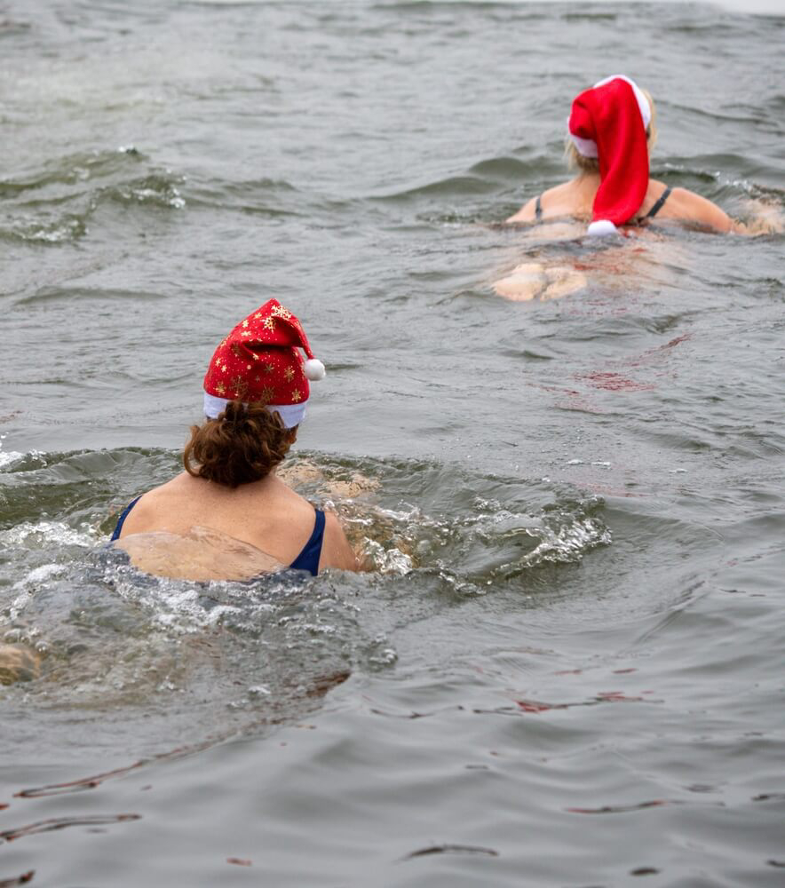 Wild Swimming: Two people in Santa Claus hats swimming in a lake in winter