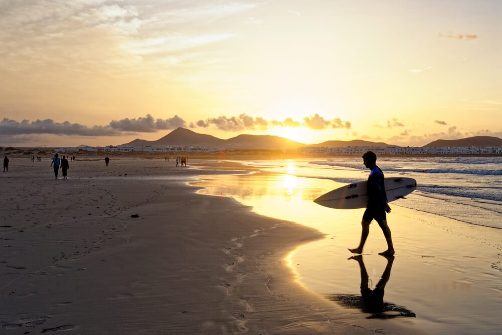 Activity holidays Lanzarote: A man walking into the sea with a surfboard