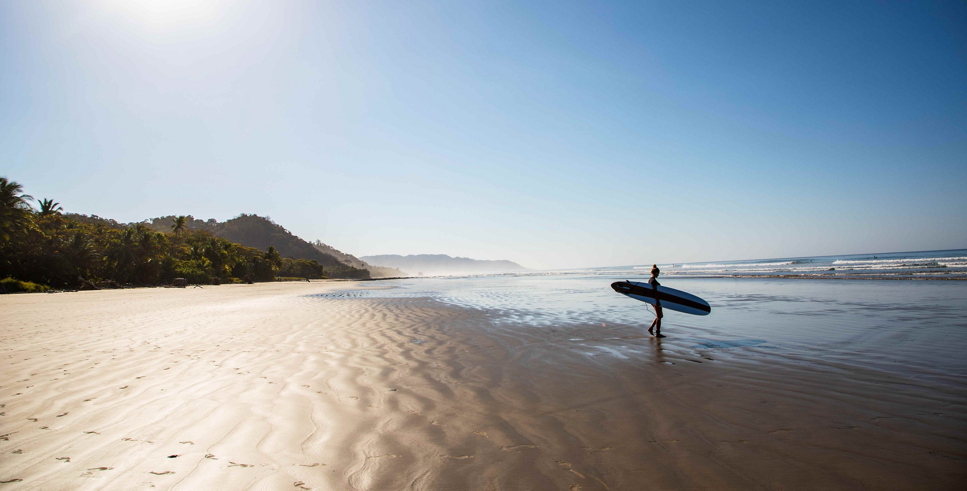 Surfen in Costa Rica: Frau mit Surfbrett an einem einsamen Strand.