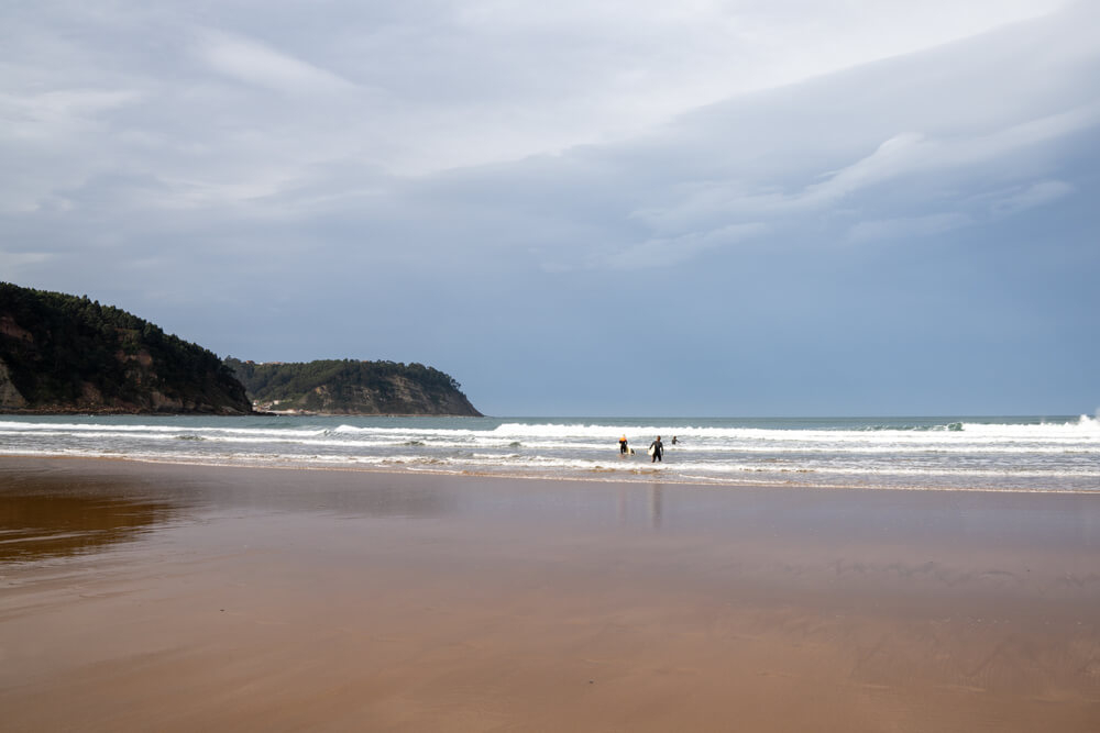 Rodiles: Golden sand, green mountains and two people surfing on Rodiles Beach