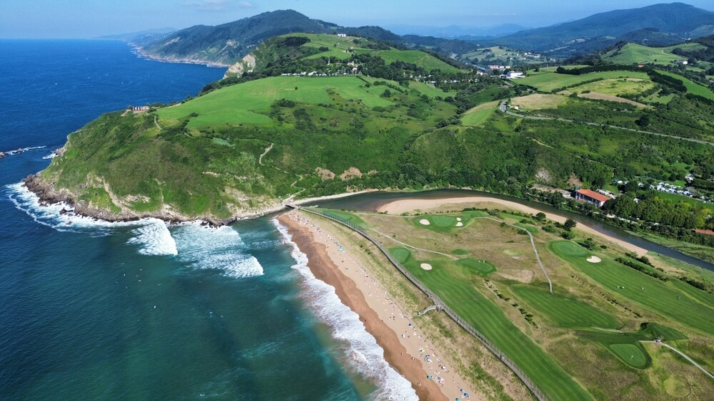 Surfing in Spain: Green headland surrounded by ocean at Zarautz Beach