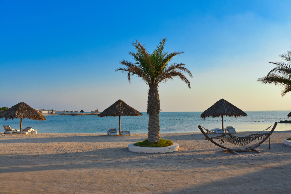 Al Dar islands: A white sand beach with parasols and the blue ocean in the distance