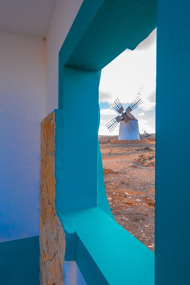 Gofio Mill: A windmill on a stone low-lying building against a volcanic setting and sea