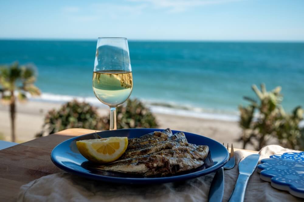 Plate of grilled sardines with a glass of white wine by the sea