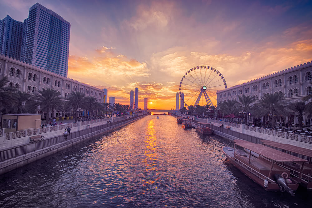 Al Qasba: A large, wide waterway with decorative buildings along the edge in purple light