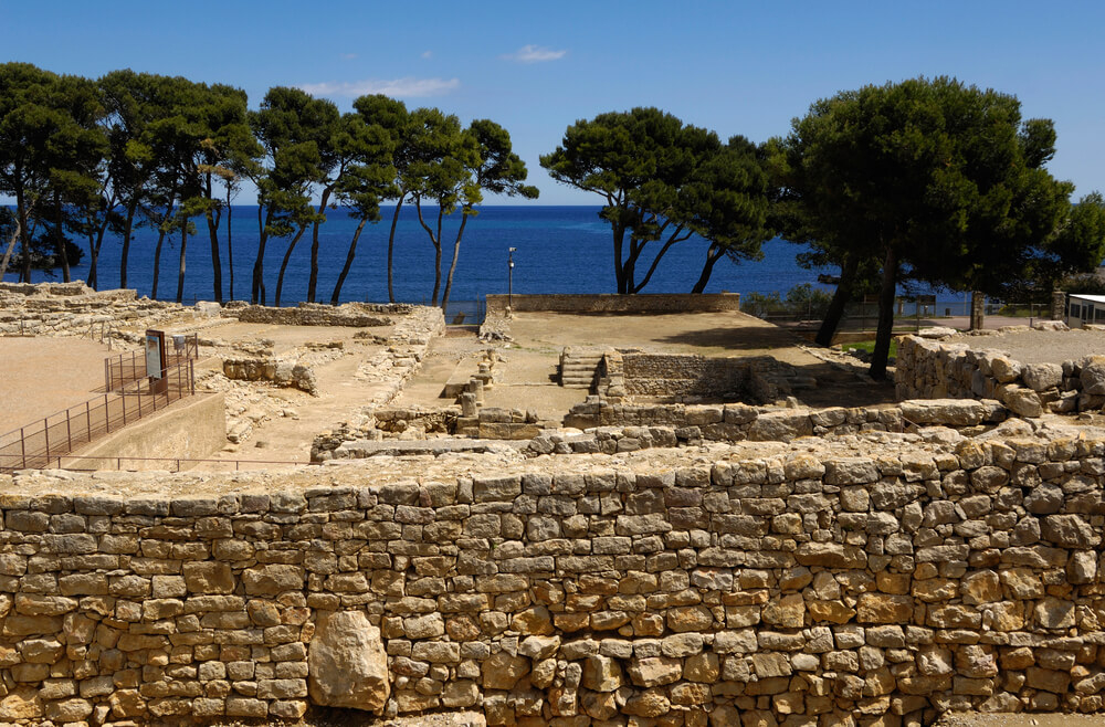 Ruins of Empúries: A sandstone archaeological site with trees and a blue sea in the distance