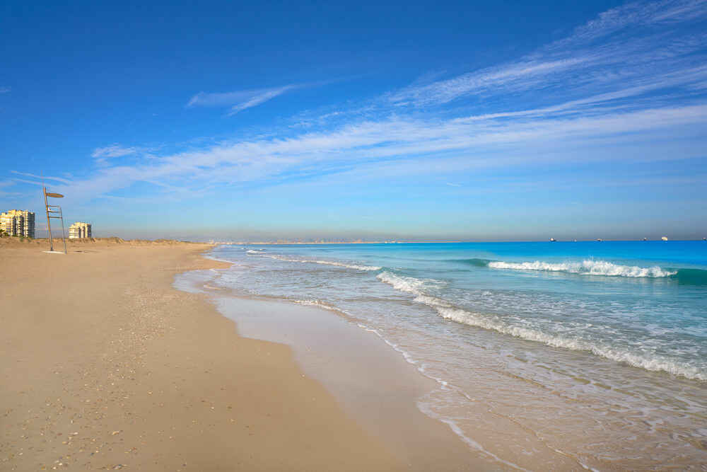 El Saler Beach: A wide golden stretch of sand and blue ocean with a sign in the distance