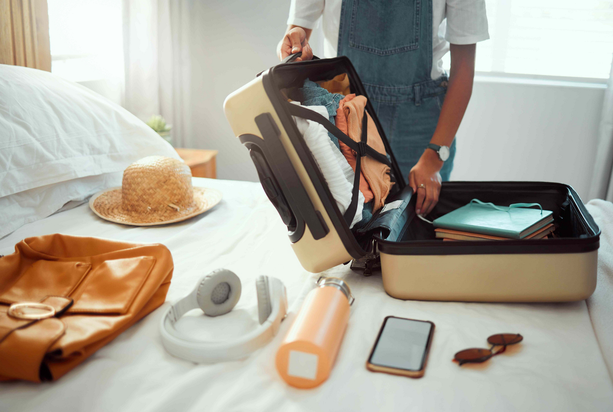 Travel Trends: Woman packing a suitcase on a white bed