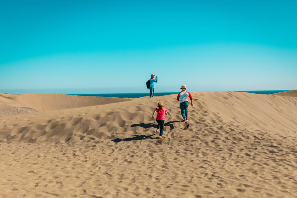 Urlaubsziele mit Kindern: Familie läuft durch die Dünen von Maspalomas in Gran Canaria.