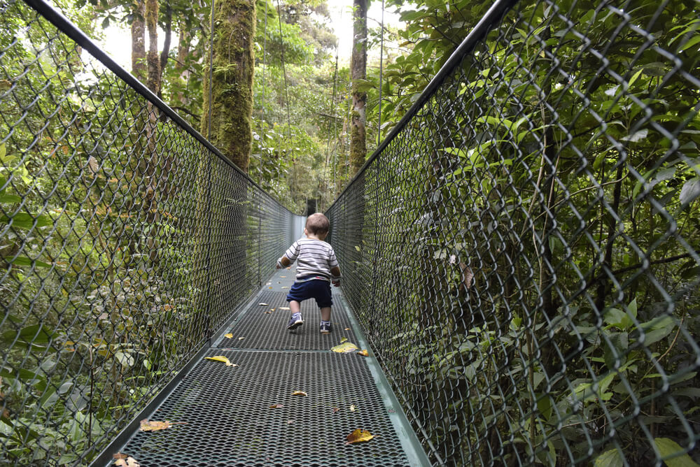 Urlaubsziele mit Kindern: kleines Kind auf einer Hängebrücke im Urwald in Costa Rica. 