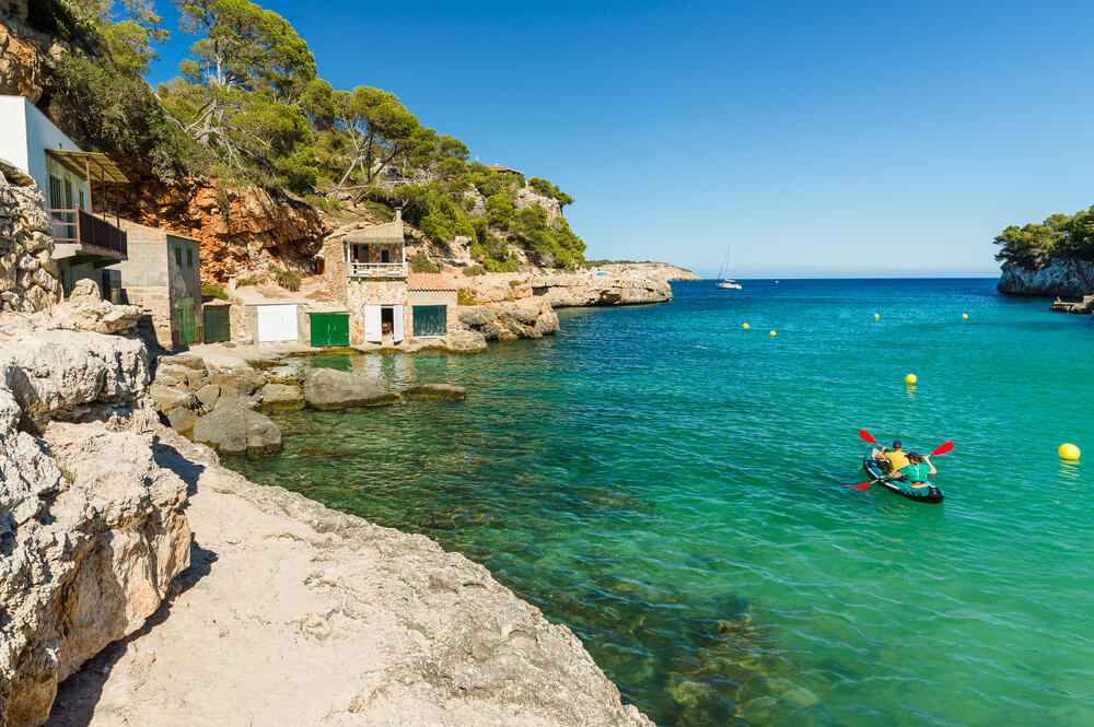 Watersports in Mallorca: A couple kayaking in a Mallorca bay with cave houses in the cliffs