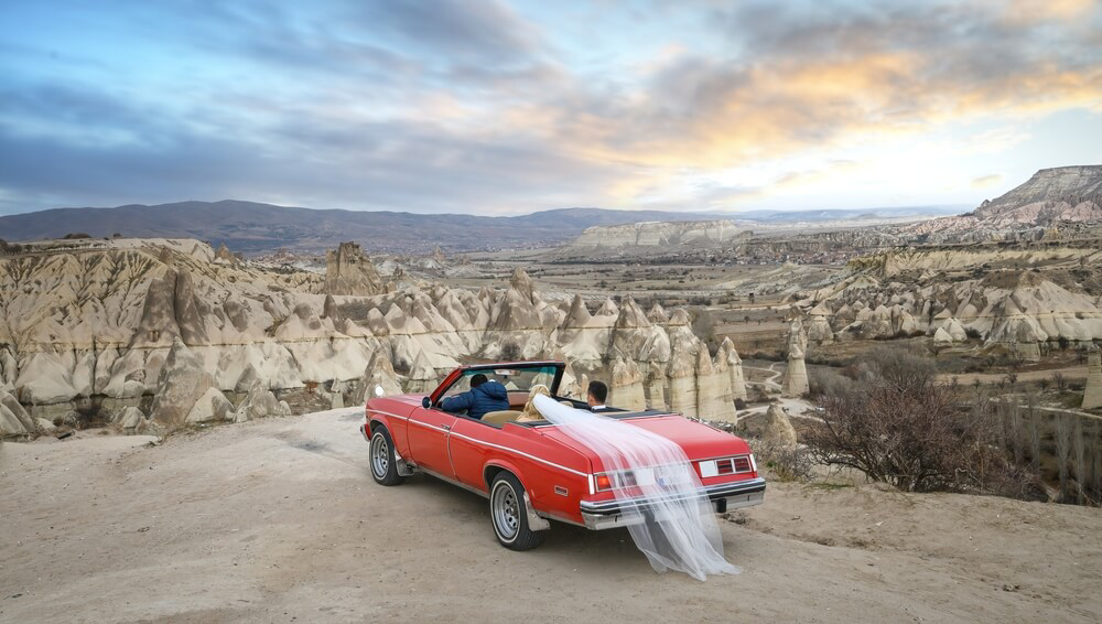 Wedding destinations: A red sports car with a bride and groom overlooking Goreme