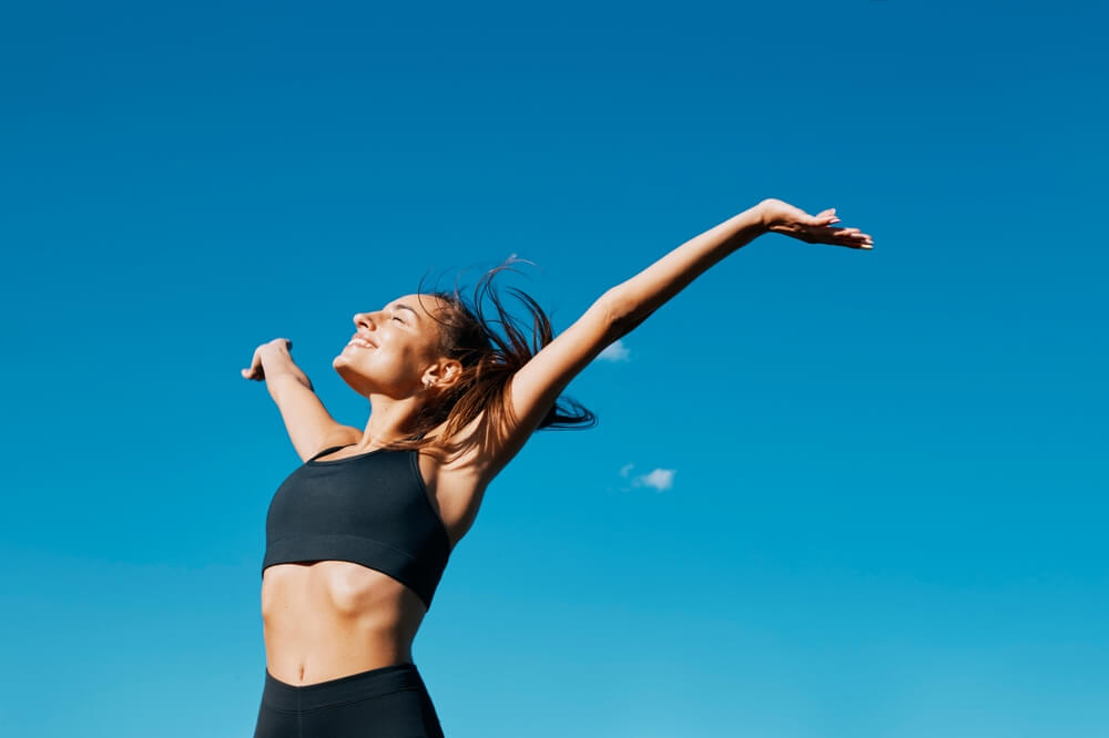 Wellness holidays: Woman in yoga wear, arms outstretched against a blue sky