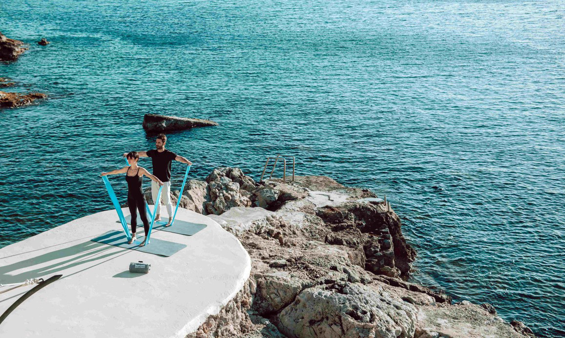 Wellbeing breaks: woman and man doing pilates on a rocky outcrop by the sea