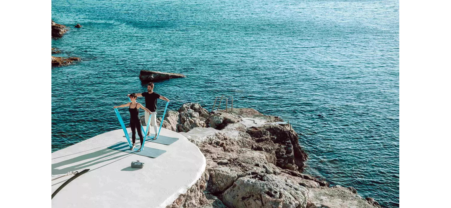 Wellbeing breaks: woman and man doing pilates on a rocky outcrop by the sea