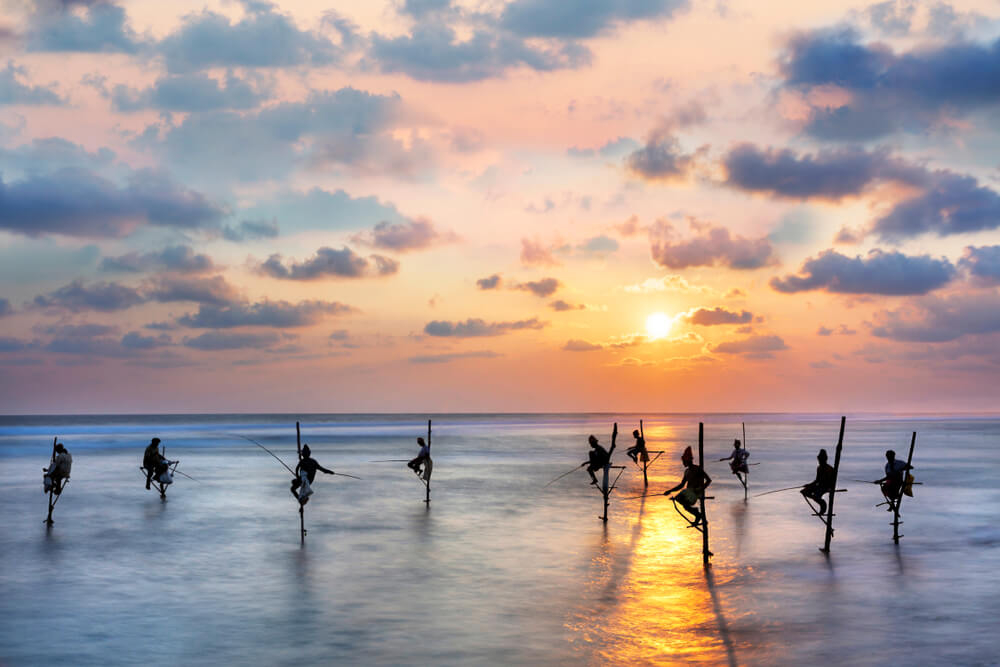 Fischer auf Stelzen an einem Strand in Sri Lanka in der Dämmerung.