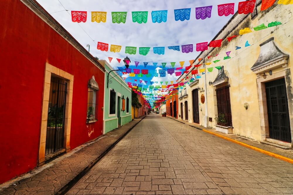 Valladolid, Yucatán, Sehenswürdigkeiten: Straße mit bunten Fassaden und Fahnen.