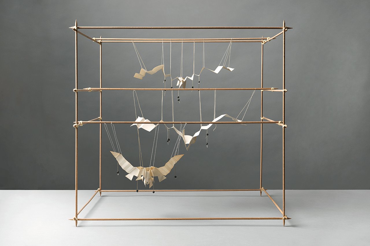Estructura cúbica de varillas metálicas con varias figuras de pájaros suspendidas en su interior.