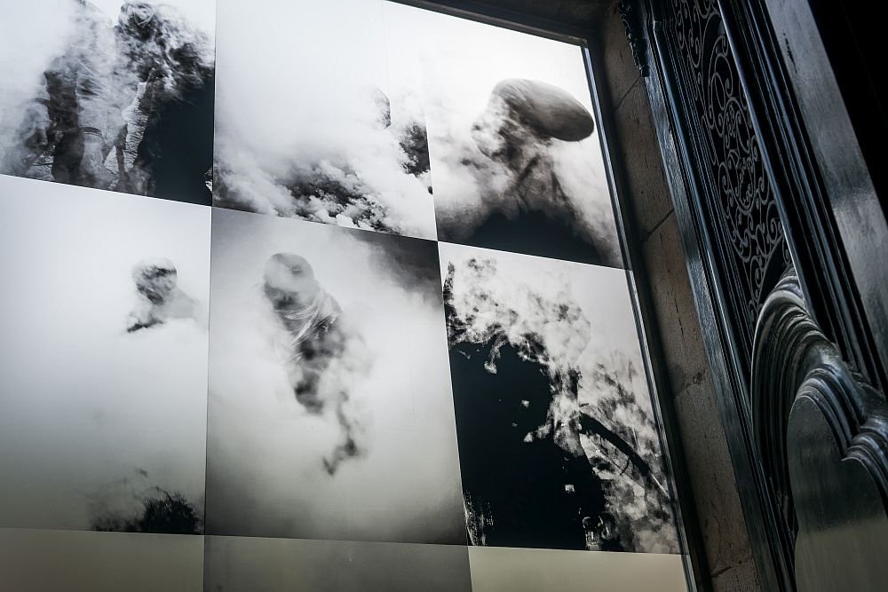 Paneles fotográficos en blanco y negro con imágenes abstractas de formas entre nubes y humo, junto a un elemento arquitectónico oscuro con relieves ornamentales.