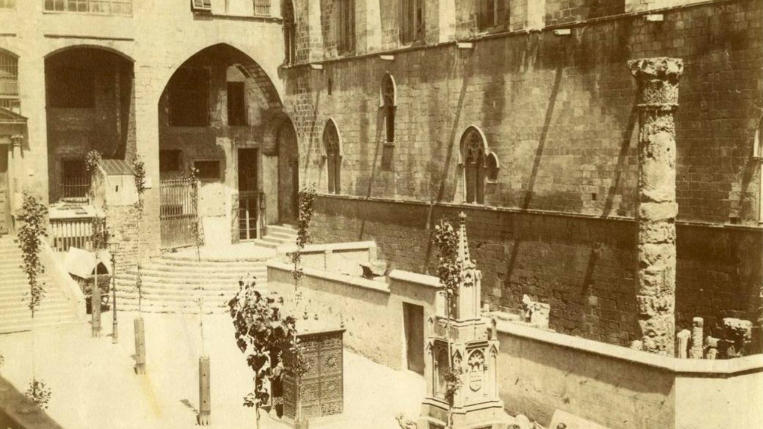 De tons sèpia, una imatge de la plaça del Rei de Barcelona. Al fons, es veuen els arcs d'entrada del Saló del Tinell i a la dreta s’alça la façana de la capella de Santa Àgata amb grans finestrals ogivals i murs robustos, amb una columna romana al davant. En  primer terme hi ha una font ornamental de pedra treballada i un grup de persones que s’aplega al carrer, vestides d’època, observant o participant en alguna escena quotidiana.