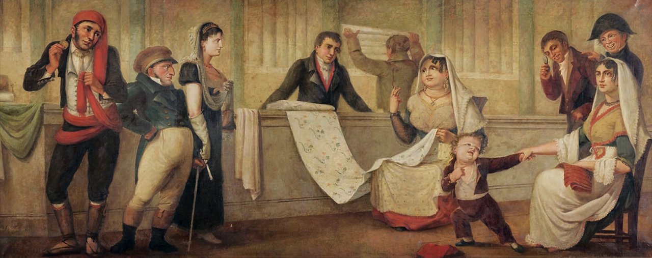 Dipinto di scena di genere con diversi personaggi in un interno. A sinistra, due uomini in abiti popolari osservano la situazione, mentre al centro c’è una donna seduta con un velo, che guarda un tessuto, circondata da figure che interagiscono con lei, come il venditore dietro il banco. Sullo sfondo, un altro personaggio maneggia un rotolo di stoffa. A destra, una donna seduta in abbigliamento tradizionale riceve l’attenzione di un bambino che la indica con un gesto vivace. La scena è piena di espressioni e gesti che suggeriscono una situazione quotidiana all’interno di una bottega di indiane.