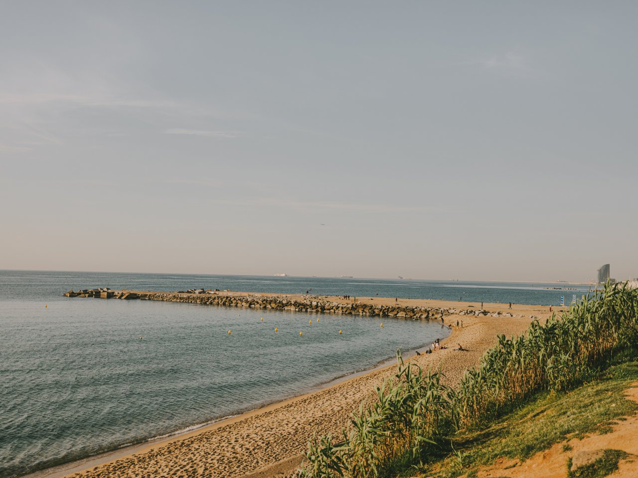 Banyistes a la platja i escullera al fons