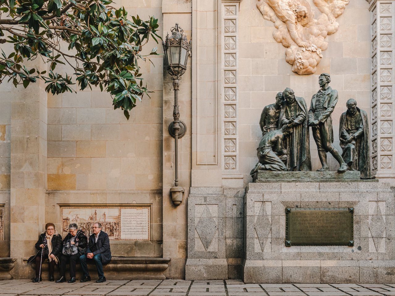 Pla general del monument amb 3 persones grans assegudes al banc al costat